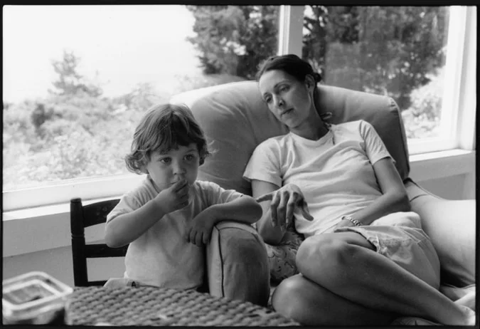 A woman and a small child sitting together on a sofa by a window