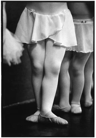 The legs and slippered feet of small children standing in third position