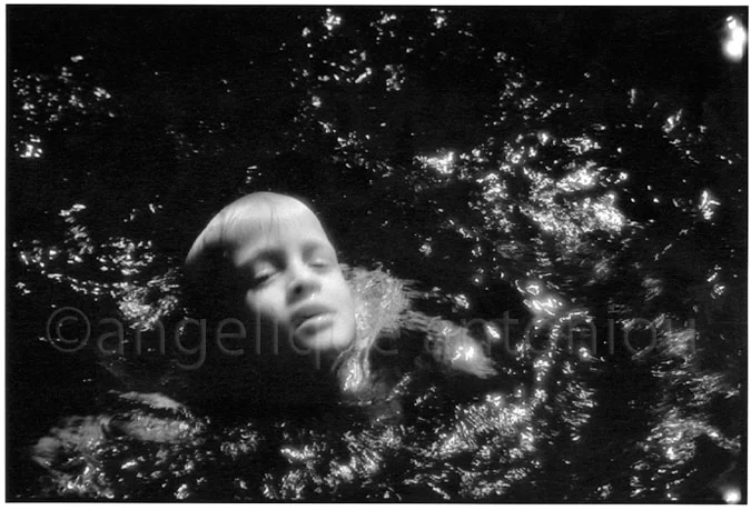 A child's face breaking the surface of dark, light-flecked water