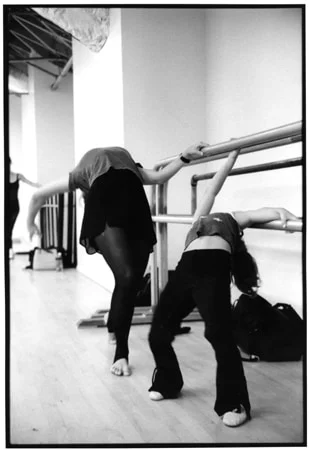 Two dancers bending backwards over the barre in a rehearsal studio