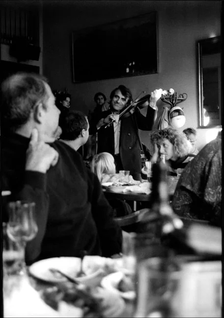 A violinist standing and playing among diners at crowded restaurant tables