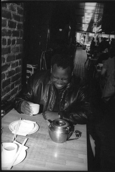 A man in a leather jacket laughing over a teapot and cups at a restaurant table