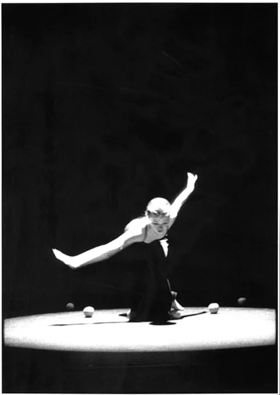 A dancer leaning far forward on a lit circular stage, one leg extended behind her