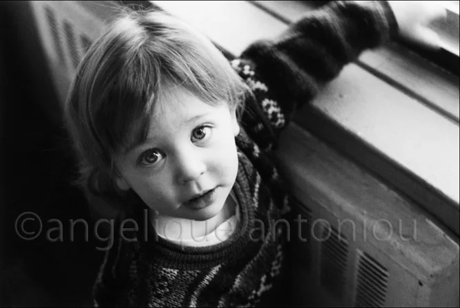 A small child in a patterned jumper looking up, leaning against a radiator