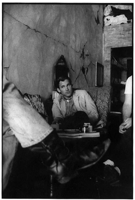 A man sitting back on a coffee-shop couch looking up, others crossing the foreground