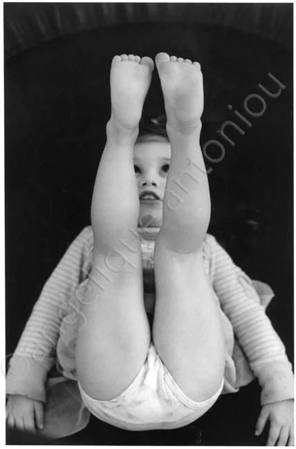 A baby lying on their back with both legs raised, the soles of their feet to the camera