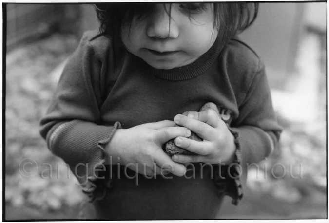 A small child cupping a stone in both hands and looking down at it