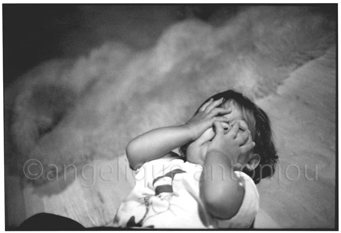 A small child lying on a sheepskin, rubbing both eyes