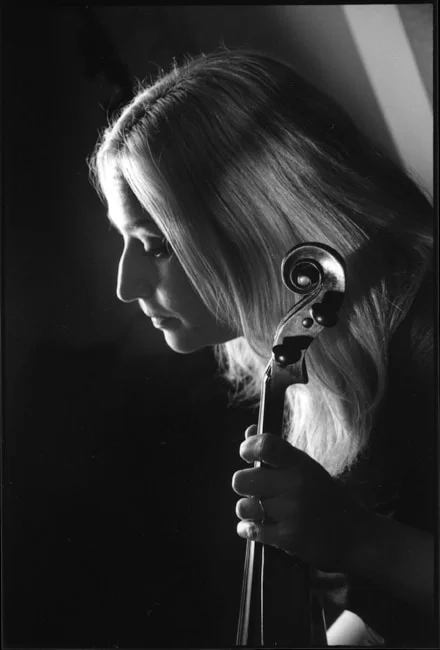 A young woman resting her cheek against the scroll of her violin in the dark