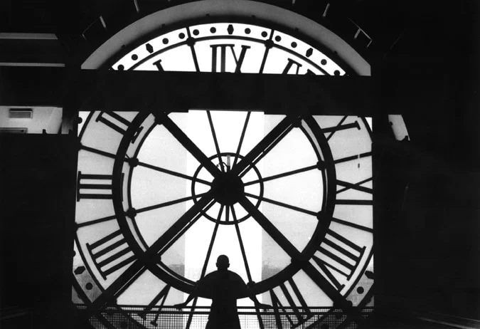 A figure standing in silhouette inside the glass of a great station clock face