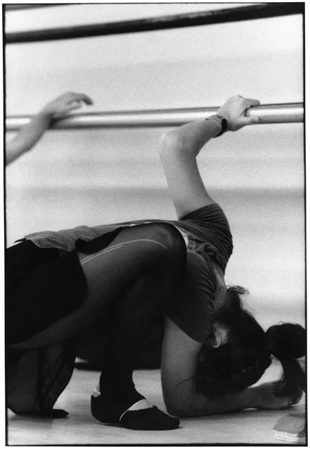 A dancer curled down to the studio floor with one hand still on the barre