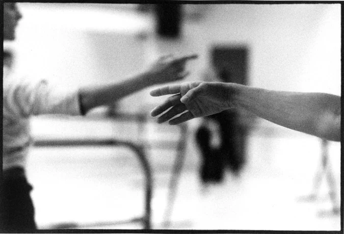 Two outstretched arms reaching towards each other across a rehearsal studio