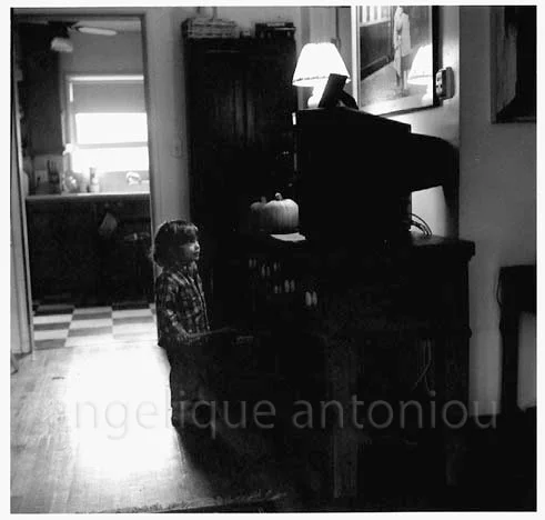 A child standing in a darkened room, kitchen light falling through the doorway behind